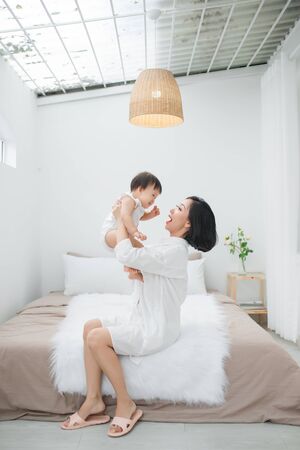 Young mother playing with her little girl at the bedroomの写真素材