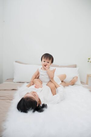 Young mother playing with her baby in bedroom at homeの写真素材