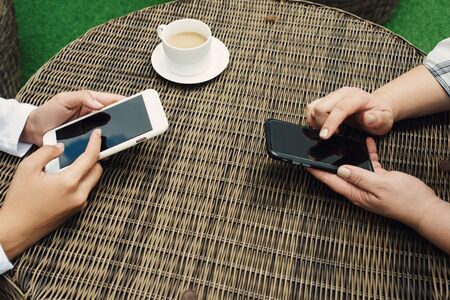 Two girls using smartphone in female hands in coffee shop. Close-upの写真素材