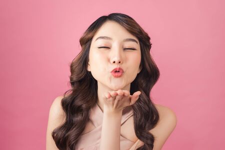 Beautiful young Asian woman blow a kiss on pink backgroundの写真素材
