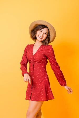 Happiness. Happy summer Asian woman isolated in studio. Energetic fresh portrait of young woman excited cheering in wearing beach hat and read dress.の写真素材
