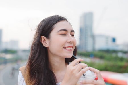 Profile view of attractive young woman with cup of coffee in hand sitting outdoors and enjoying view of modern city.の写真素材
