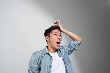 Portrait of a Asian man holding his head with his hand and suffering from headache, in a jeans t-shirt on a white backgroundの写真素材