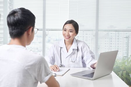 Beautiful female doctor in white medical coat is consulting her patientの写真素材