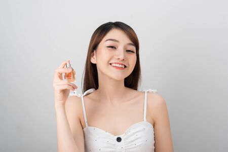 A beautiful woman of Asian appearance smiles into the camera and holds in her hand a jar of liquid with a scent of charm perfumeの写真素材