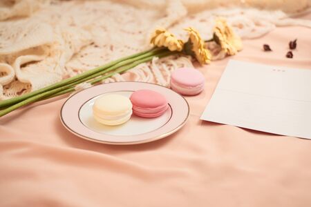 Envelope, flowers, and macarons with cup of tea on light background