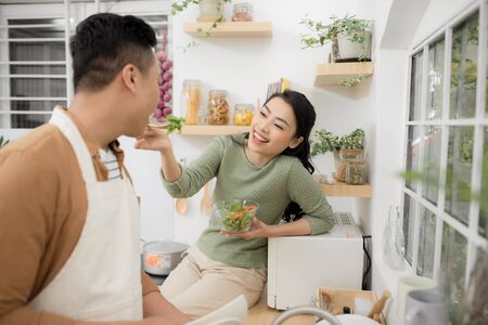 Loving woman feeding man while cooking dinner at kitchen.の写真素材