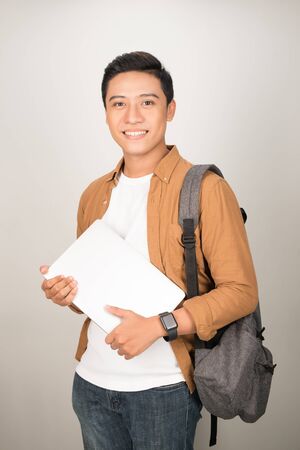 Portrait of Asian teenage college boy holding books and documents against white backgroundの写真素材
