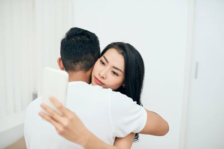 Young couple in the bedroom. An attractive woman is checking incoming messages in the morningの写真素材