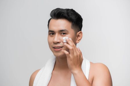 smiling man applying cosmetic cream on face,の写真素材