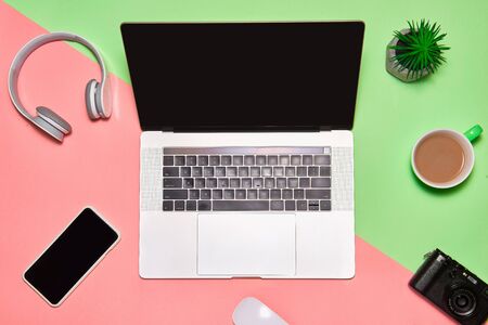 Desk table with laptop, coffee cup, headphones and camera on color tableの写真素材