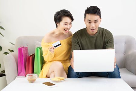 Portrait of a cheerful couple shopping online with laptop computer while sitting at the table at homeの写真素材