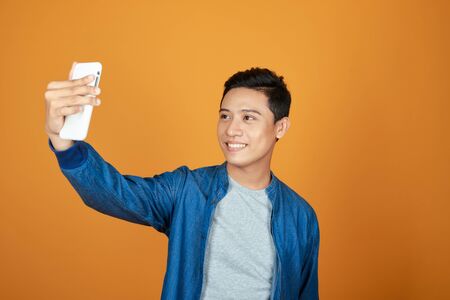 Young happy Asian man selfie with smartphone in colorful orange background