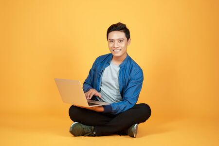 Asian man use of the laptop computer against color orange backgroundの写真素材