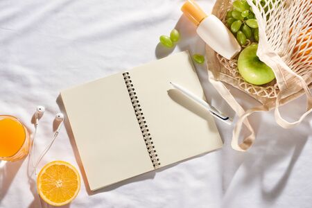 Notebook with fruit, sun cream, bag on white fabric background.