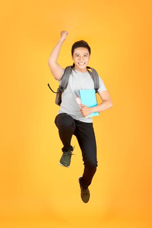 Excited young Asian man jumping with a backpack on the an orange backgroundの写真素材