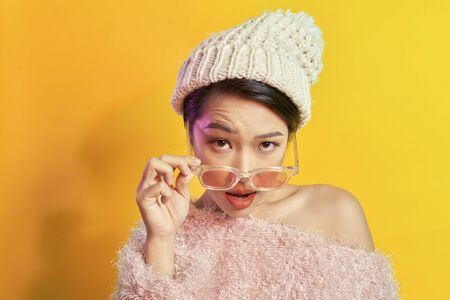 Emotional asian girl with colorful makeup posing on yellow background with eyeglasses. Indoor photo of amazed woman in trendy fur coat.の写真素材