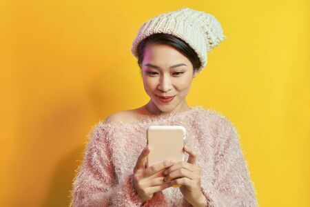 Elegant young woman in sunglasses and wears soft fur coat looking at phone screen.
