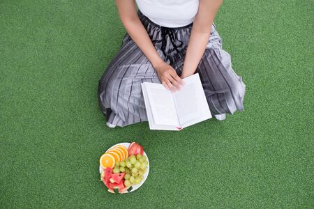 Relaxing moments, Young woman reading a book while sitting on the grass.の写真素材