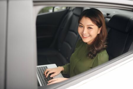 Beautiful businesswoman using laptop while sitting on a backseat of a car.の写真素材