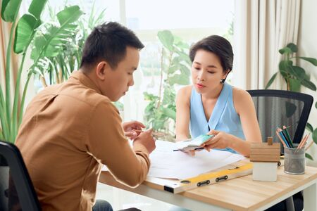 Finding solution together. Confident young man and woman looking at blueprint together while both standing in officeの写真素材