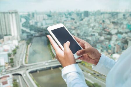 Female hand holding, using smartphone on cityscape with high riseの写真素材