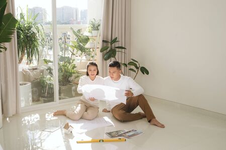 repair, building, renovation and people concept - close up of happy couple looking at blueprint at homeの写真素材