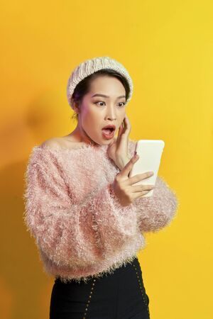 Shocked girl looking at phone screen with mouth open. Outdoor portrait of surprised young woman  wearing pink fur attire and holding smartphone.の写真素材