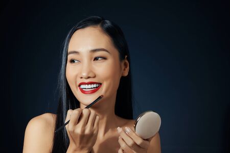 Makeup artist applies red lipstick. Beautiful female face. Hand of a make-up master painting lips of a young girl beauty model. Makeup in progressの写真素材