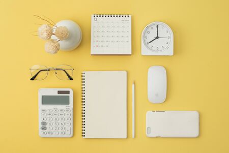 Notebook, mouse, phone, calculator, glasses, pen, calendar, alarm on yellow background. Flatlay, top view.の写真素材