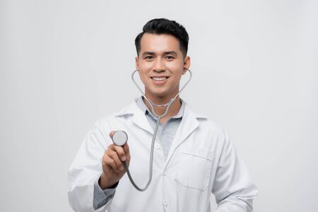 Portrait of a friendly handsome male doctor dressed in uniform holding stethoscope and looking at camera isolated over white backgroundの写真素材