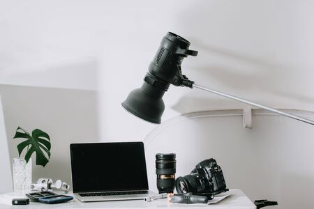 Still life working from home desk with professional photographic equipment, camera, lens, computer monitor, electronics indoors.の写真素材