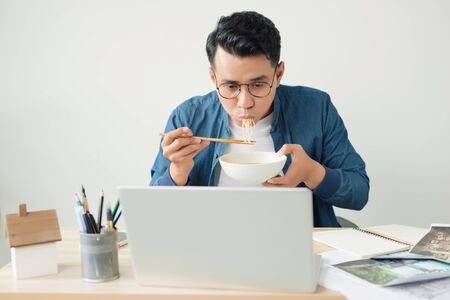 Young asian architect eating noodle at office. On desktop