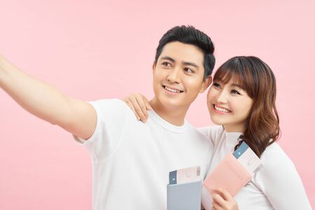 happy asian man and woman holding passports and air tickets while looking at camera isolated on pinkの写真素材