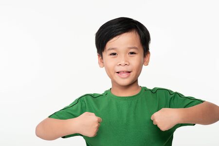 Portrait of cute smart young Asian boy shows winning gesture and smiling at camera, celebrating success victory against white backgroundの写真素材
