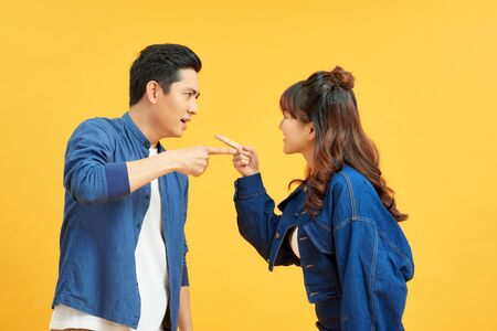 Photo of irritated aggressive couple man and woman screaming at each other while standing face to face isolated over yellow backgroundの写真素材