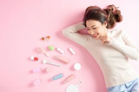 Smiling Asian woman lying on pink background with her cosmetics tools. Top viewの写真素材