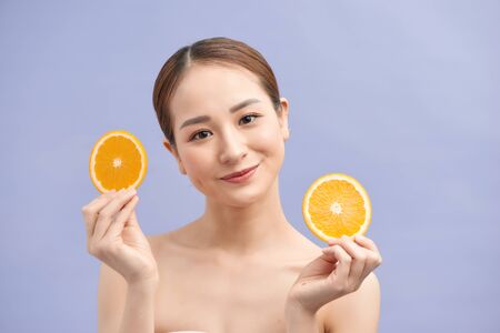 Amused fresh asian woman holding two oranges slices on violet backgroundの写真素材