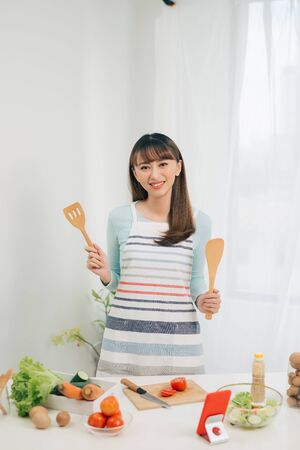 Beautiful young asian woman reading cooking recipe or watching show while making saladの写真素材