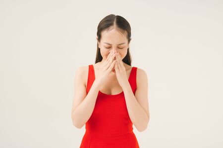 Beautiful woman in a red dress closed her nose with both hands isolated on a white backgroundの写真素材