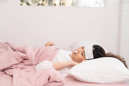 Portrait of a beautiful young woman lying in bed, having a cold and sneezing in a tissue.の写真素材