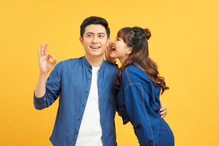 Young couple two friends guy girls posing isolated on yellow orange wall background. People lifestyle concept. Mock up copy space. Whispering secret behind handの写真素材