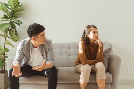 Upset couple at home. Handsome man and beautiful young woman are having quarrel. Sitting on sofa together. Family problems.の写真素材