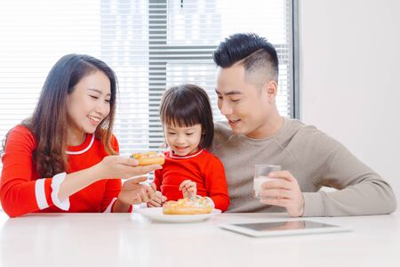 Happy young family with children enjoying breakfast in a white sunny dining roomの写真素材