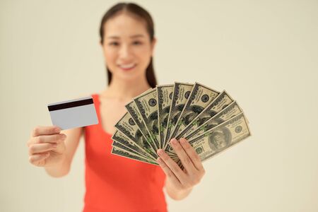 Excited young woman with cash money and credit card on gray background