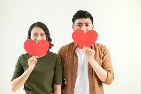 Beautiful young loving couple is holding a card in the shape of heart over white background.の写真素材
