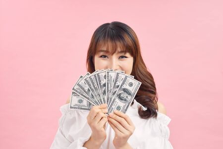 Portrait of a joyful woman showing dollars and showing gestures on a pink background.の写真素材
