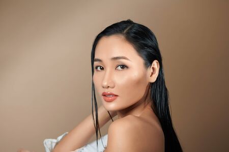 Fashion studio photo of gorgeous sexy woman with luxurious dark hair on beige backgroungの写真素材