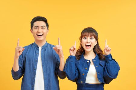 Young beautiful couple standing over isolated yellow background amazed and surprised looking up and pointing with fingers and raised arms.の写真素材