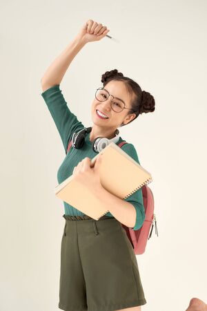Beautiful student girl wearing backpack holding notebook over isolated white backgroundの写真素材
